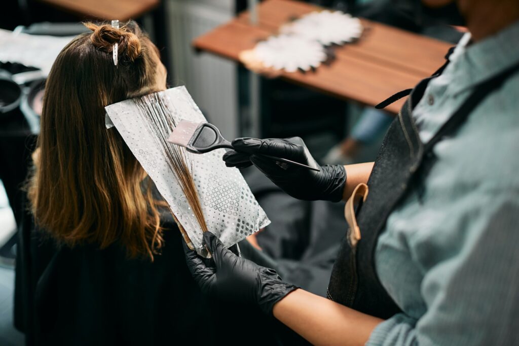 Close-up of hairdresser dyeing customer's hair at the salon.