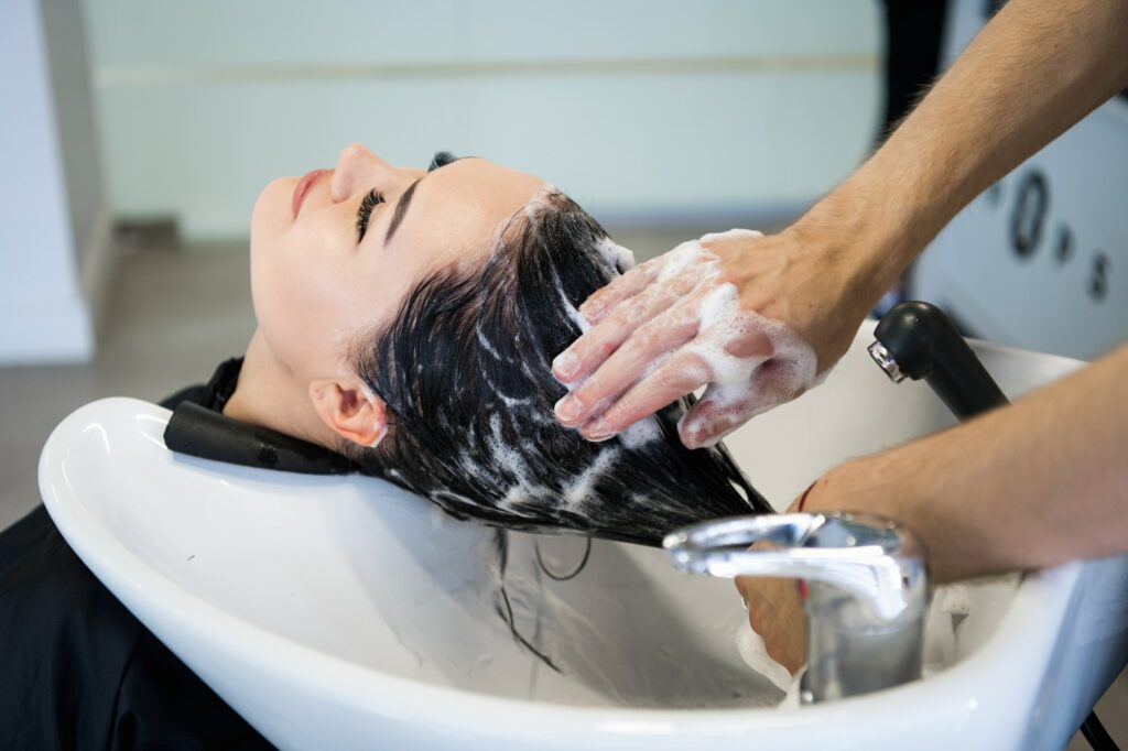 Unrecognizable professional hairdresser washing hair to her client. Beautiful hairdresser washing